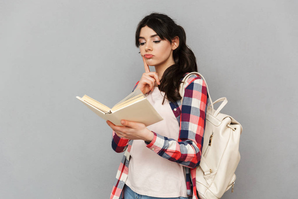 Image of thinking young lady student standing isolated over grey background wall reading book. - Foto, Imagem
