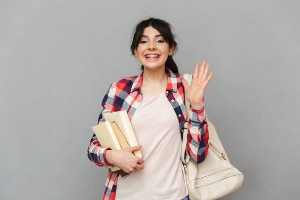 Image of happy young lady student standing isolated over grey background wall holding books. - Φωτογραφία, εικόνα
