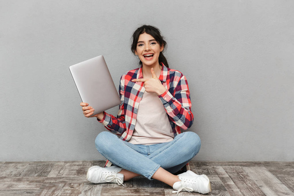Image of happy young lady student isolated over grey background wall holding laptop computer pointing. - Zdjęcie, obraz