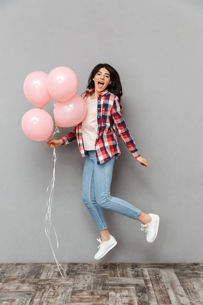 Image of cute beautiful young lady jumping isolated over grey background wall holding balloons. - Foto, afbeelding