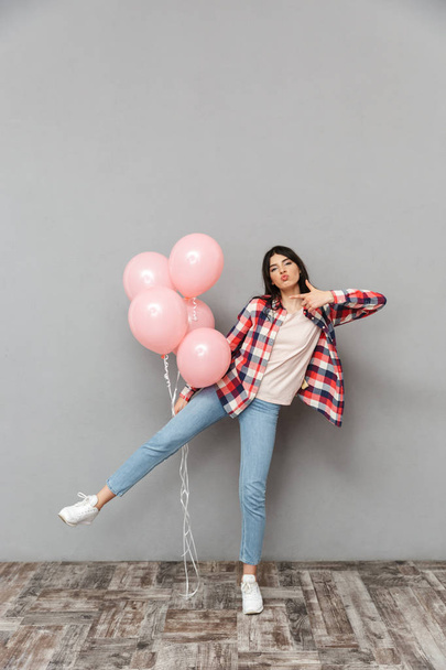 Image of cute beautiful young lady standing isolated over grey background wall holding balloons pointing. - Foto, afbeelding