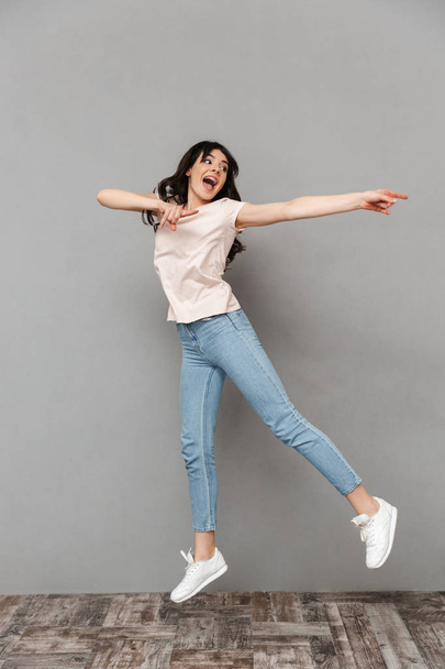 Photo of excited young lady jumping isolated over grey background wall pointing aside. - Photo, image