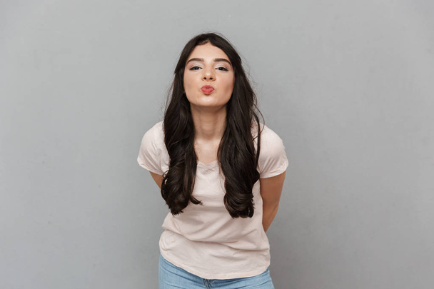 Photo of cute pretty young lady standing isolated over grey background wall looking camera blowing kisses. - Foto, Imagem
