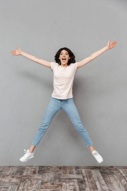 Image of emotional young lady jumping isolated over grey background wall. - 写真・画像