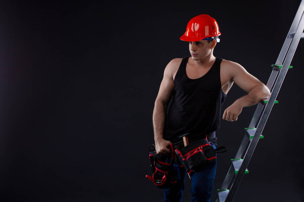 Il lavoratore si appoggia su una scala e alza lo sguardo su uno sfondo nero. atleta casco
 - Foto, immagini