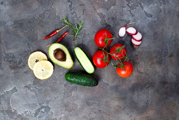 Verse biologische ingrediënten voor de salade maken: avocado, tomaten, radijs, komkommer, citroen, peper op steen donkere achtergrond, bovenaanzicht. Flat lag met plaats voor tekst. Vegan en gezond voedsel concept - Foto, afbeelding
