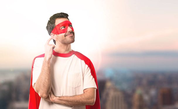 Supersankari mies naamio ja punainen viitta seisoo ja ajatella idea raapimalla päätä auringonlaskun taustalla
 - Valokuva, kuva