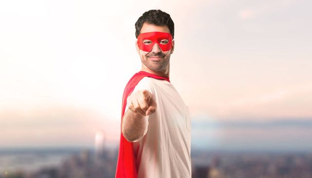 スーパー ヒーロー マスクと赤のケープと男が夕日を背景に自信を持って式にあなたに指をポイントします。 - 写真・画像