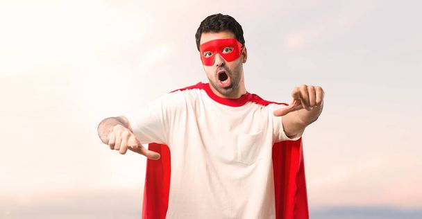 Uomo supereroe con maschera e mantello rosso che punta con il dito a qualcuno e ride molto su uno sfondo tramonto
 - Foto, immagini