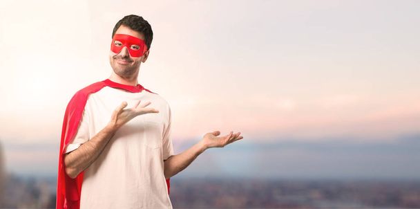 Uomo supereroe con maschera e mantello rosso che estende le mani di lato e sorridente per la presentazione e l'invito a venire su uno sfondo tramonto
 - Foto, immagini