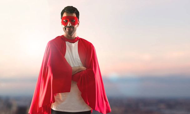 Süper kahraman maske ve kırmızı pelerin kolları adamla günbatımı bir arka plan üzerinde çarpı işareti - Fotoğraf, Görsel