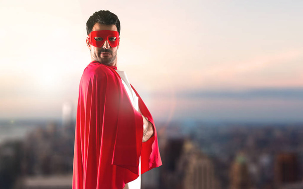 Superhero człowiek z maska i czerwona Peleryna z rękami skrzyżowanymi na tle zachodu słońca - Zdjęcie, obraz