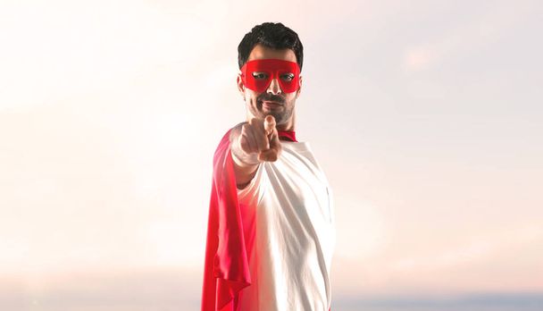 Hombre superhéroe con máscara y capa roja apuntando al frente sobre un fondo al atardecer
 - Foto, imagen