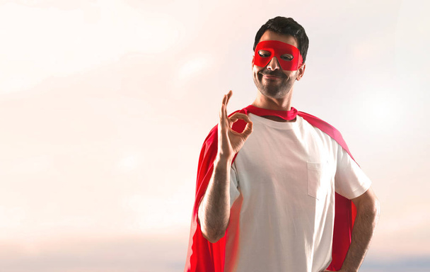 スーパー ヒーロー マスクと赤マントは、夕日を背景に署名 [ok] を作る男 - 写真・画像