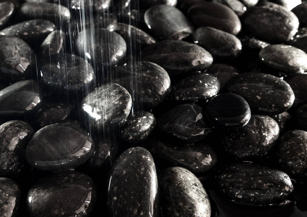 Superficie brillante de piedra negra redonda en el suelo junto a la cascada
 - Foto, Imagen