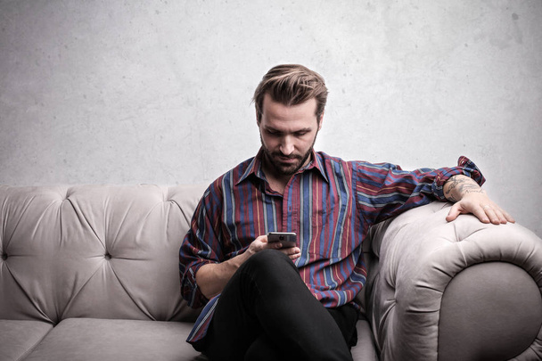 Young charming man using his smartphone on a sofa. - Foto, Imagen