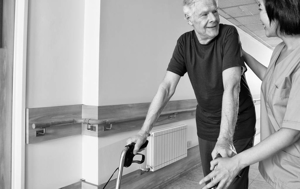 Hastane koridorunda hemşire konuşurken walker ile mutlu yaşlı adam. - Fotoğraf, Görsel