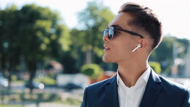 Attractive young businessman talking on the phone using wireless earphones walking outside. Happy man talks. Communication, finance, business people, interns, CEO. Close up. Shot on Red Epic - 映像、動画
