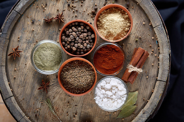 Spices in ceramic bowls on the top of wooden barrel, close-up, selective focus, vertical. - Foto, afbeelding