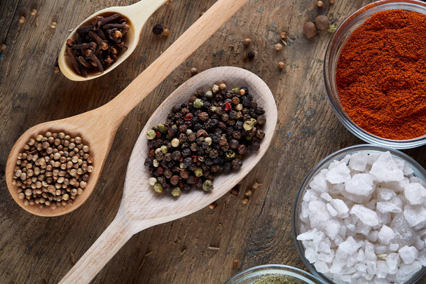 Various spices in wooden spoons and bowls and some salt on an old wooden barrel, top view, close-up, selective focus. - Foto, Imagen