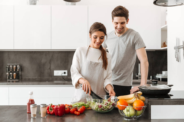 Portrait of a cheerful young couple cooking together at the kitchen - Foto, immagini