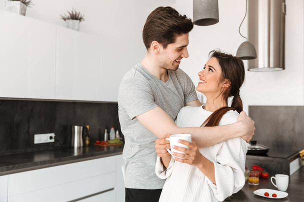 Portrait of a pretty young couple drinking coffee at the kitchen at home - Foto, Imagem