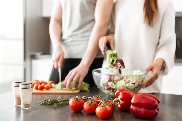 Close up portrait of a young couple cooking salad together at the kitchen - Foto, Bild