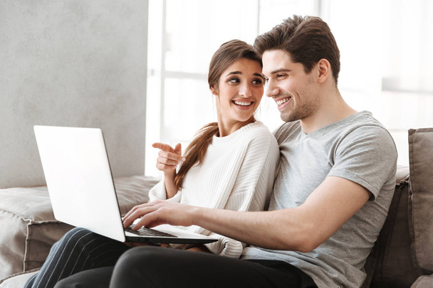 Portrait of a smiling young couple using laptop computer while sitting on a couch at home - Фото, зображення