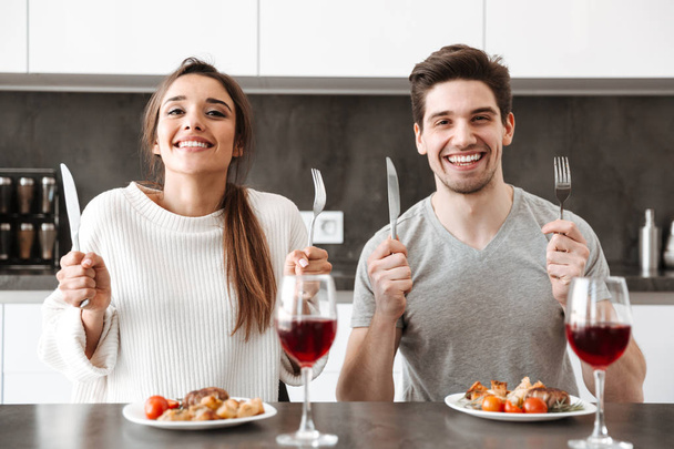 Portrait of a happy young couple sitting at the kitchen table and having dinner - Foto, immagini