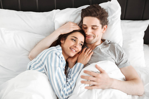 Portrait of a happy young couple lying together in bed - Fotografie, Obrázek