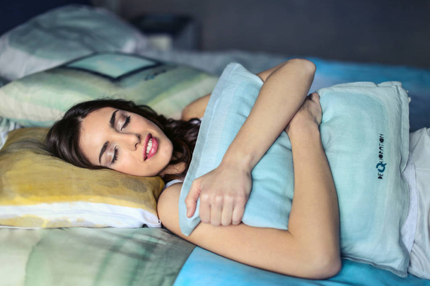 Beautiful woman hugs her pillow while sleeping in her bed. - Valokuva, kuva
