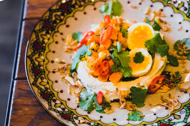 Hummus, salsa ghanoush baba con huevos escalfados, perejil y chile. Aperitivo tradicional de Oriente Medio. Placa adornada colorida
 - Foto, imagen