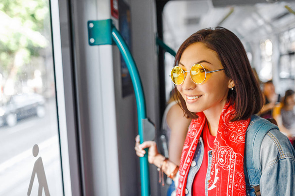 Uma mulher asiática com óculos está sentada em um bonde ou ônibus, conceito de transporte público
 - Foto, Imagem