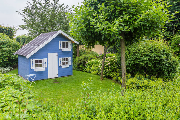 Затишний маленький ігровий будиночок в зеленому саду
 - Фото, зображення