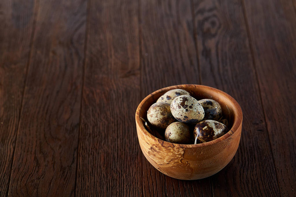 Fresh quail eggs in a wooden bowl on a dark wooden background, top view, close-up - Foto, Bild