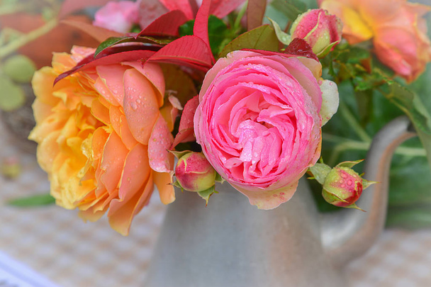 Pink and yellow roses in a metal teapot on a table for decor - Foto, Bild