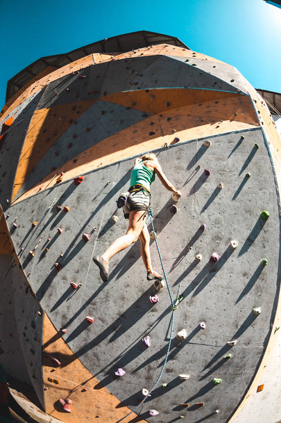 Der Bergsteiger trainiert auf einem künstlichen Relief. Eine Frau klettert auf einer Straßenkletterwand eine Kletterroute hinauf. Training in der Halle. Fischaugenobjektiv. - Foto, Bild