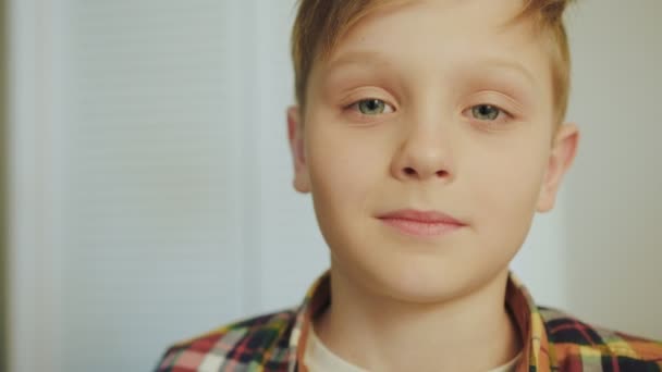 Portret van de schattige blonde jongen in het geruite shirt kijken naar de camera en oprecht glimlachen. Witte muur achtergrond. Close-up. Binnenshuis - Video
