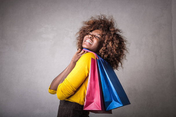 Joven mujer afro sonriendo felizmente con bolsas de compras en la mano
. - Foto, imagen