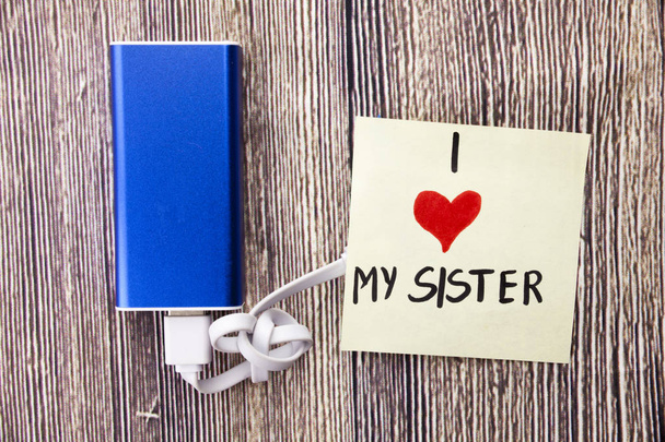 blue power bank charging with white data cable kept on the wood table written on the page i enormously love my sister that he told us all things present perfectly here . - Φωτογραφία, εικόνα