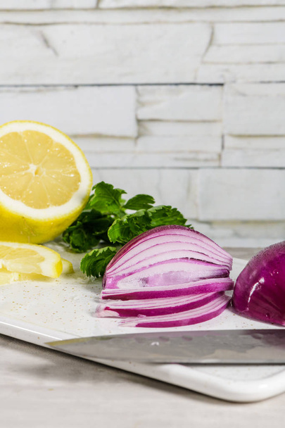 Sliced red onion, lemon and parsley leaves on white ceramic cutting board. - Fotografie, Obrázek