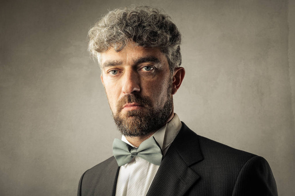 Homem de negócios de cabelos encaracolados com laço olhando a sério
. - Foto, Imagem