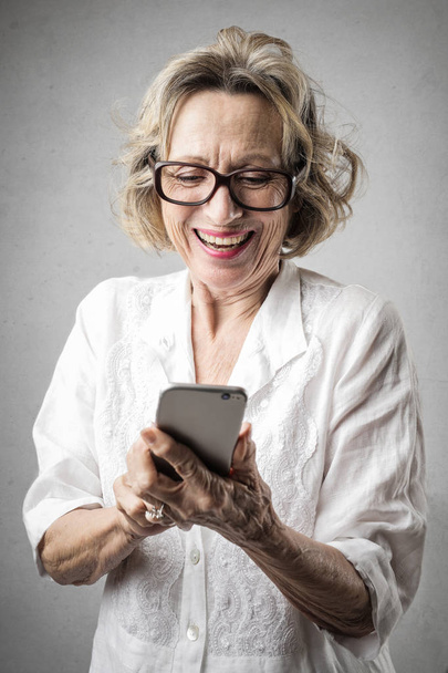 Senior femme élégante avec des lunettes vérifier heureusement son smartphone
. - Photo, image