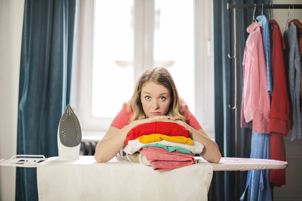 Young pretty woman feeling overwhelmed and looking sad with her laundry. - Foto, afbeelding