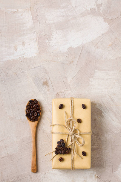 Craft gift box with twine and coffee heart shape decoration wooden spoon with coffee beans on beige concrete background. Gift decor idea for coffee lovers. Top view flat lay place for copy space text. - Photo, Image