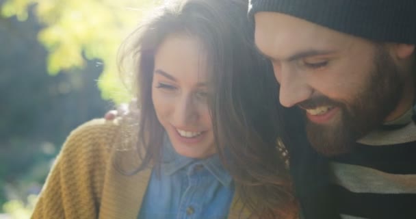 Close up of young attractive couple sitting closely to each other and looking carefully down on something. Portrait. Park in the sunny fall. Outside - Footage, Video