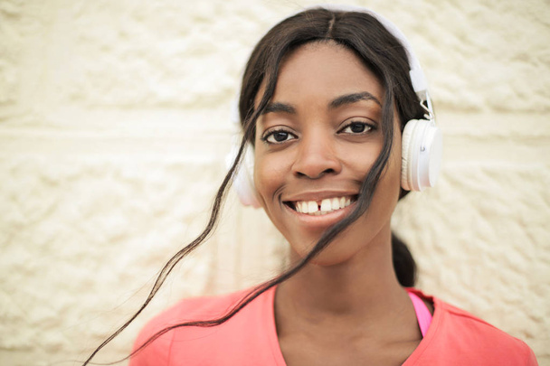 Young beautiful Afro woman with headphones smiling positively into the camera outdoor. - Фото, изображение