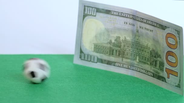 Fotbalový míč zasáhne sto dolarové bankovky na zeleném pozadí. Pojem peněz a fotbalu, prodávající vítězství a porážka, sport a bohatství, korupce a sportovní obchod. - Záběry, video