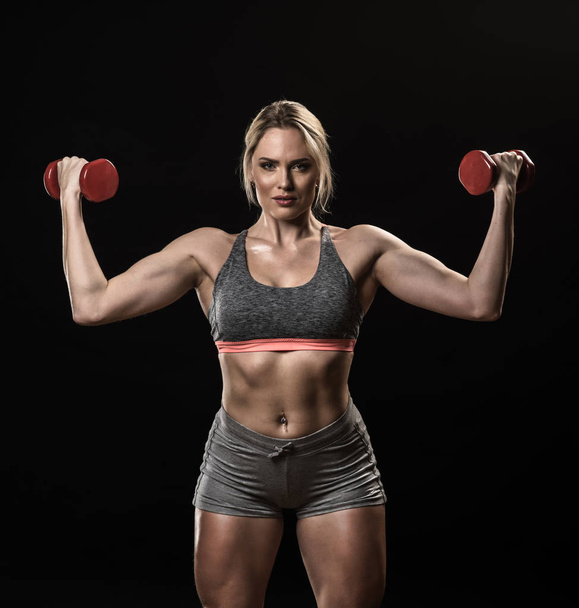 Beautiful muscular woman lifting dumbbells isolated on black background - Фото, изображение