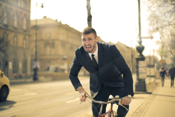 Young businessman in suit riding a bike fast in the city. - Фото, изображение